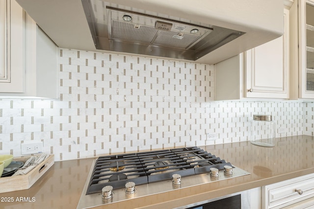 kitchen featuring light countertops, stainless steel gas stovetop, glass insert cabinets, exhaust hood, and backsplash