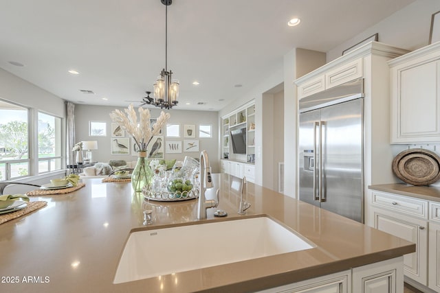 kitchen featuring stainless steel built in refrigerator, open floor plan, white cabinets, and a sink