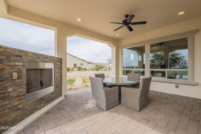 view of patio featuring outdoor dining area, an outdoor stone fireplace, and a ceiling fan