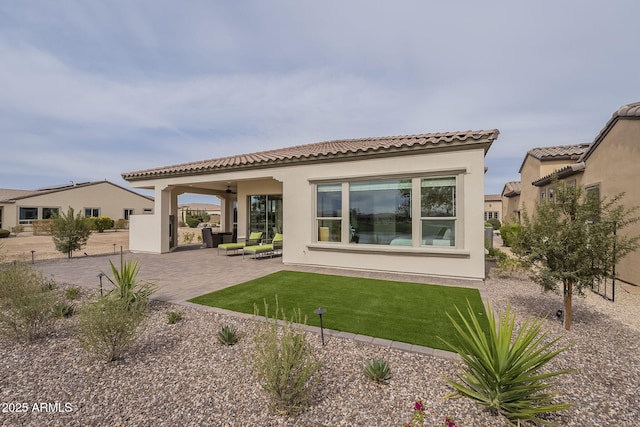 exterior space with stucco siding, a ceiling fan, a patio, a yard, and a tiled roof