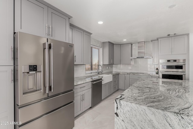 kitchen with stainless steel appliances, sink, wall chimney exhaust hood, light stone countertops, and gray cabinets