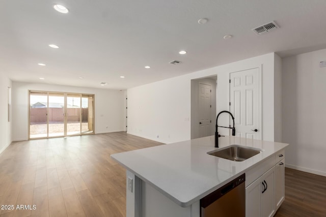 kitchen with sink, dishwasher, white cabinetry, light hardwood / wood-style floors, and an island with sink