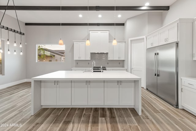 kitchen with stainless steel built in fridge, white cabinets, hanging light fixtures, and light wood-type flooring