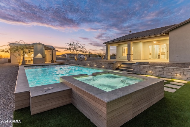 pool at dusk with an in ground hot tub and a patio