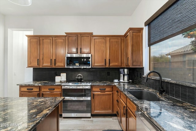 kitchen with a sink, backsplash, appliances with stainless steel finishes, and dark stone countertops