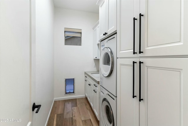 washroom with cabinet space, stacked washer and clothes dryer, light wood finished floors, and baseboards