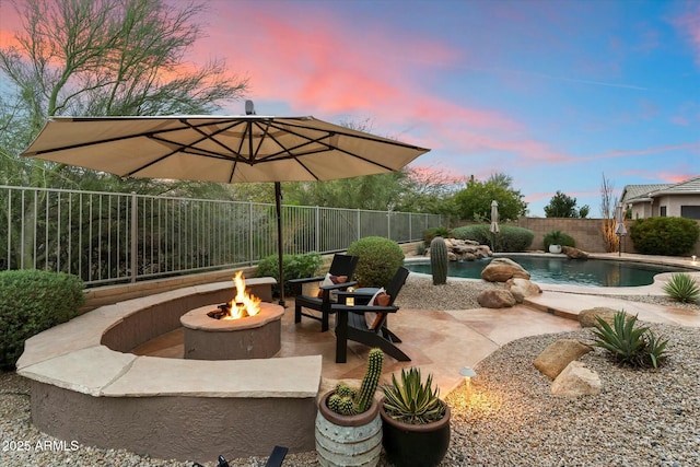 patio terrace at dusk featuring a fenced backyard, a fenced in pool, and a fire pit