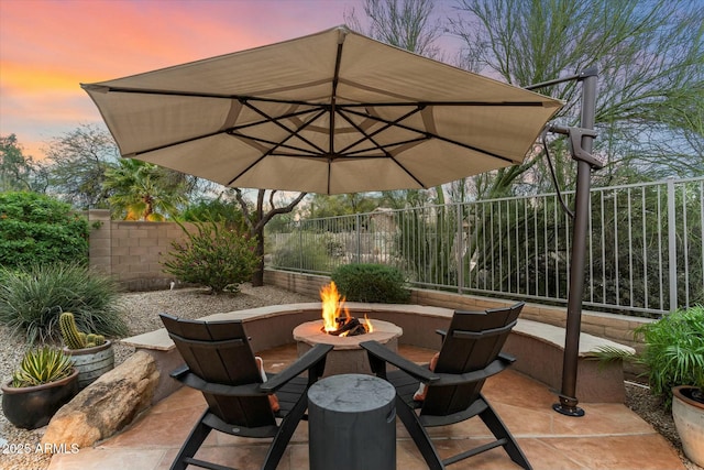 patio terrace at dusk featuring an outdoor fire pit and a fenced backyard