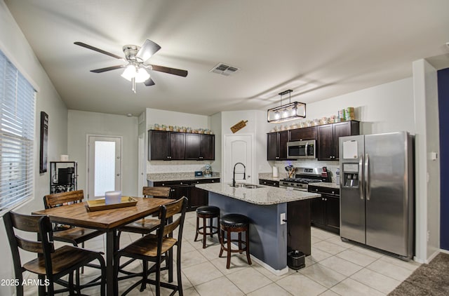 kitchen with light tile patterned floors, a sink, appliances with stainless steel finishes, a kitchen bar, and tasteful backsplash