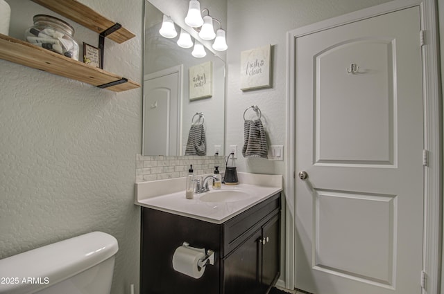 bathroom with tasteful backsplash, toilet, vanity, and a textured wall