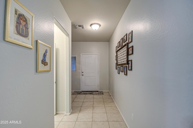 hall featuring light tile patterned floors, baseboards, visible vents, and a textured ceiling