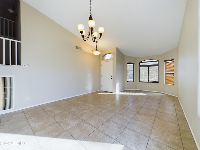 tiled empty room featuring lofted ceiling and a notable chandelier