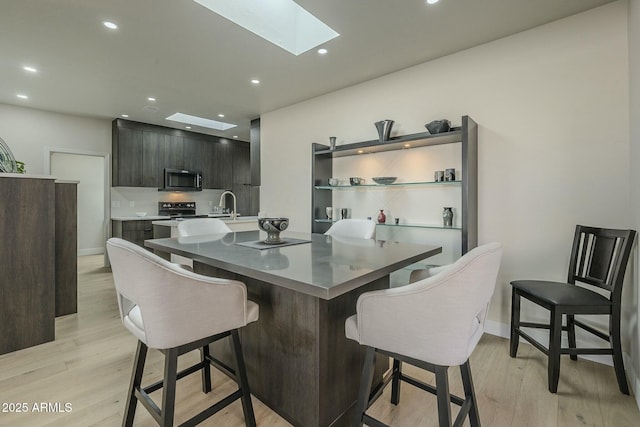 kitchen featuring sink, a breakfast bar area, a skylight, electric range, and light hardwood / wood-style floors