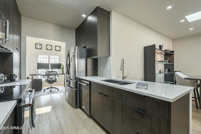 kitchen featuring a skylight, sink, fridge, dark brown cabinetry, and light wood-type flooring