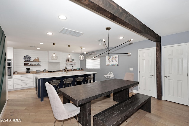 dining space featuring beamed ceiling, light wood-type flooring, and an inviting chandelier