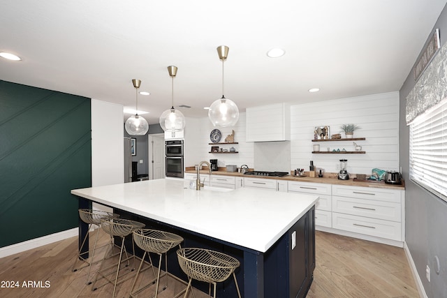 kitchen featuring sink, decorative light fixtures, light hardwood / wood-style flooring, white cabinetry, and an island with sink