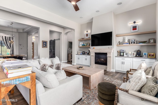 living room with a fireplace, dark hardwood / wood-style floors, a barn door, built in shelves, and ceiling fan