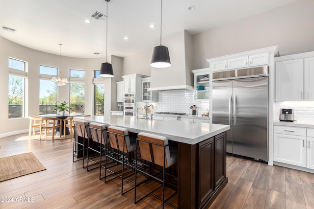 kitchen with hanging light fixtures, stainless steel appliances, wood-type flooring, and white cabinets