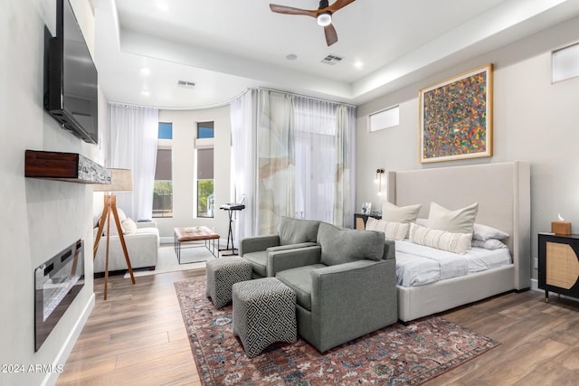 bedroom with a tray ceiling, wood-type flooring, and ceiling fan