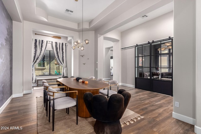 dining area featuring a barn door, a tray ceiling, and dark hardwood / wood-style flooring