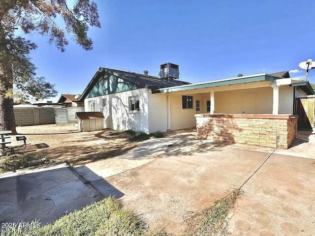 back of house with fence, central AC, stucco siding, stone siding, and a patio