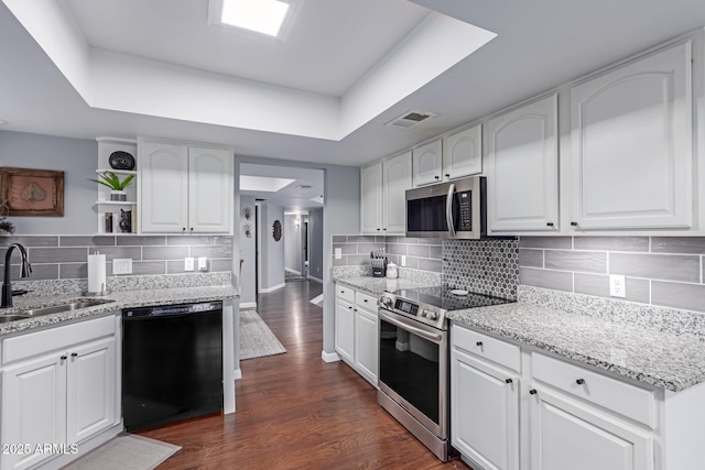 kitchen featuring visible vents, a sink, a tray ceiling, stainless steel appliances, and dark wood-style flooring