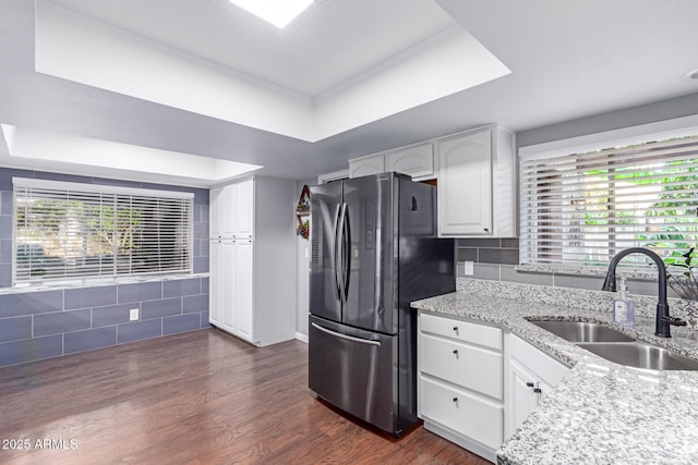 kitchen with a sink, a tray ceiling, light stone counters, dark wood finished floors, and freestanding refrigerator
