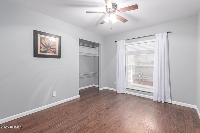 unfurnished bedroom with a ceiling fan, dark wood-style floors, baseboards, and a closet
