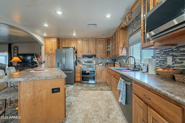 kitchen featuring sink, appliances with stainless steel finishes, a kitchen island, tasteful backsplash, and a kitchen bar