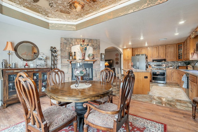 dining area with ornamental molding, a stone fireplace, sink, and light hardwood / wood-style flooring