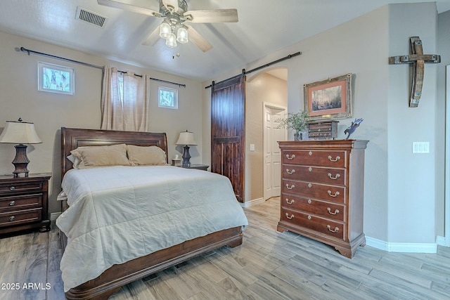 bedroom with ceiling fan, a barn door, and light hardwood / wood-style flooring