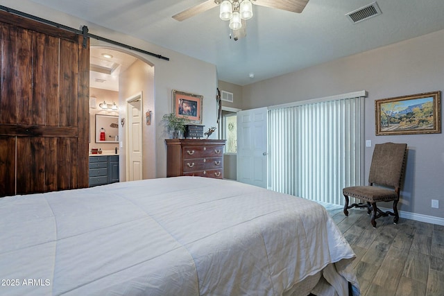 bedroom featuring ceiling fan, ensuite bathroom, a barn door, and hardwood / wood-style floors