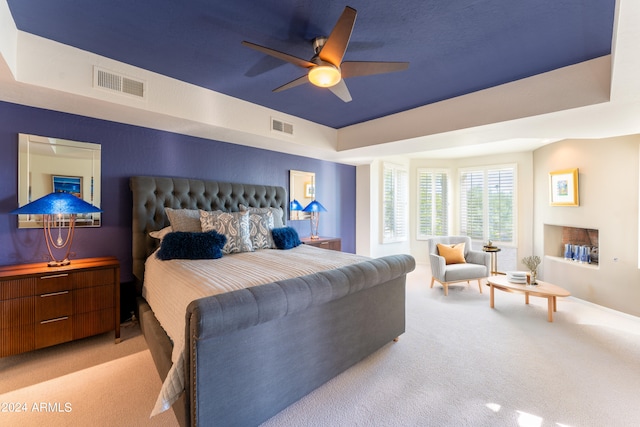 bedroom with ceiling fan, light colored carpet, and a raised ceiling