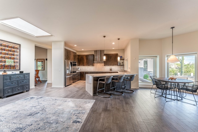 kitchen featuring a kitchen bar, decorative backsplash, light hardwood / wood-style floors, kitchen peninsula, and dark brown cabinets