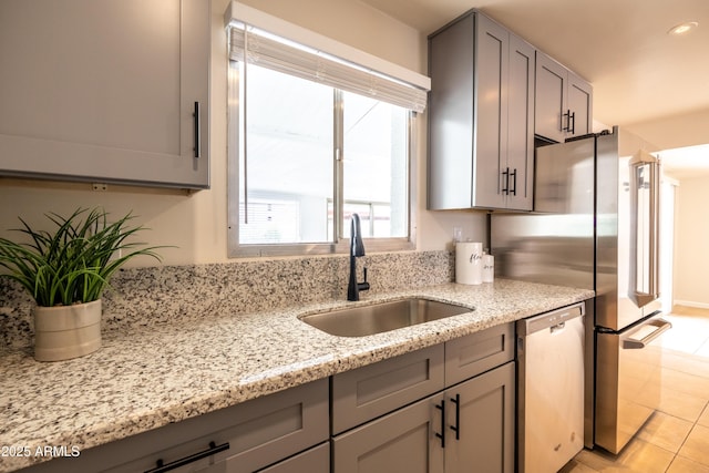 kitchen with a sink, light stone countertops, stainless steel dishwasher, and gray cabinetry