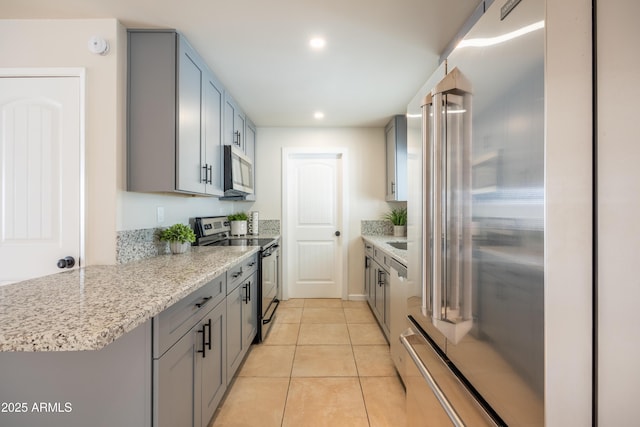 kitchen featuring light stone counters, light tile patterned floors, gray cabinetry, and stainless steel appliances