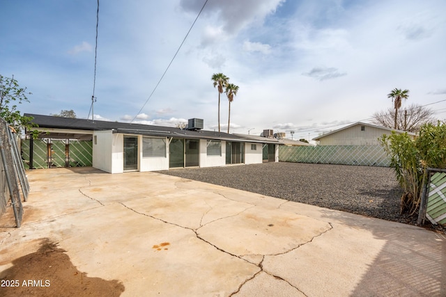 rear view of house with fence, concrete driveway, an attached carport, central AC unit, and a patio area