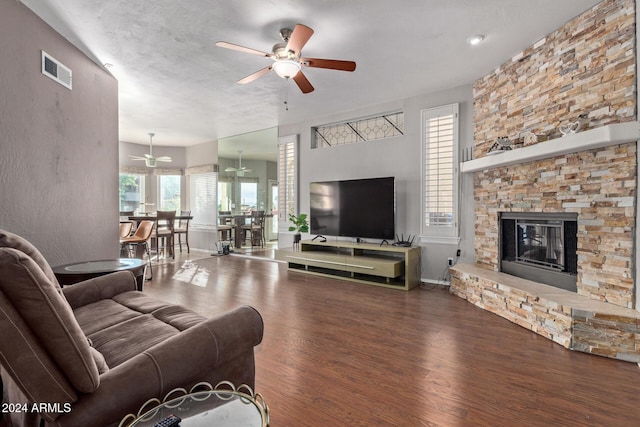 living room featuring ceiling fan, dark hardwood / wood-style floors, and a stone fireplace