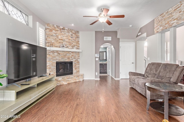 living room featuring hardwood / wood-style floors, ceiling fan, and a stone fireplace