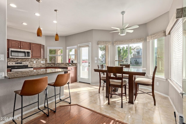 kitchen featuring ceiling fan, stainless steel appliances, tasteful backsplash, dark stone countertops, and decorative light fixtures