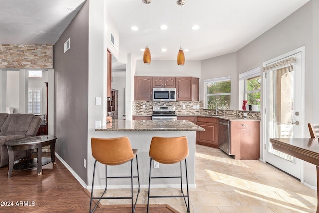 kitchen with tasteful backsplash, stainless steel appliances, sink, pendant lighting, and stone counters