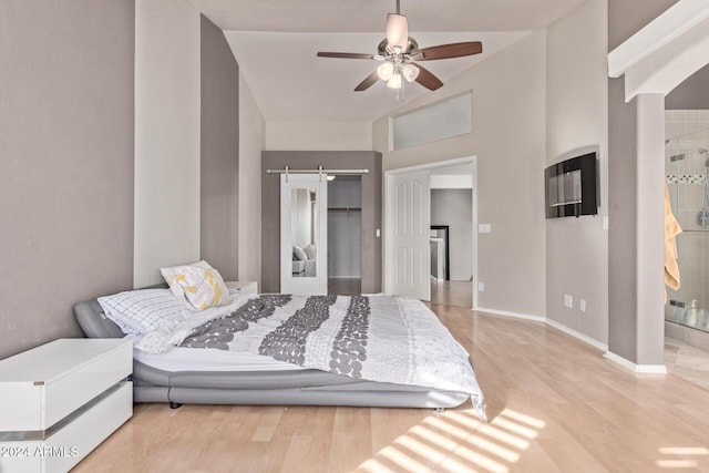 bedroom featuring light wood-type flooring, a barn door, a closet, and ceiling fan