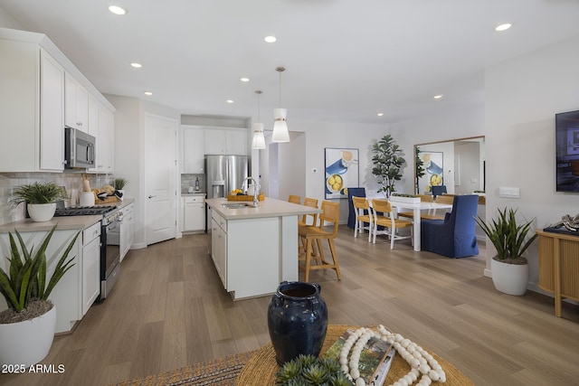 kitchen featuring white cabinetry, hanging light fixtures, backsplash, a kitchen island with sink, and appliances with stainless steel finishes