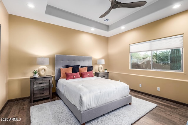 bedroom featuring a raised ceiling, wood finished floors, baseboards, recessed lighting, and ceiling fan