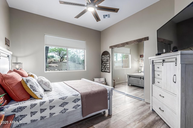bedroom featuring multiple windows, light wood-style floors, connected bathroom, and a ceiling fan