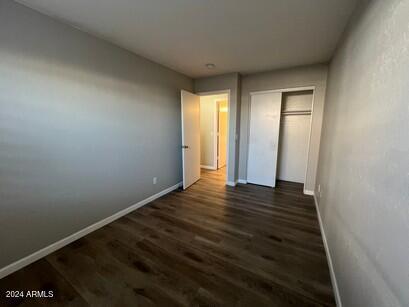 unfurnished bedroom featuring dark wood finished floors, baseboards, and a closet