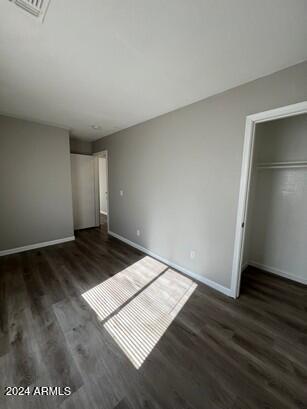 unfurnished bedroom with wood finished floors, visible vents, a closet, and baseboards