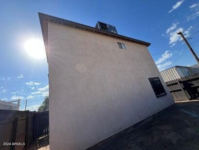 view of side of property featuring stucco siding, central AC unit, and fence