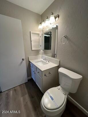 bathroom featuring toilet, wood finished floors, baseboards, vanity, and a textured wall