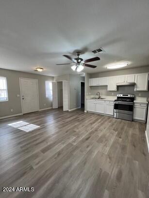 kitchen with a sink, stainless steel electric stove, wood finished floors, and white cabinetry